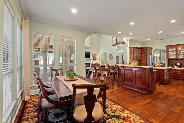 dining area featuring arched walkways, ornamental molding, dark wood-style flooring, a fireplace, and recessed lighting