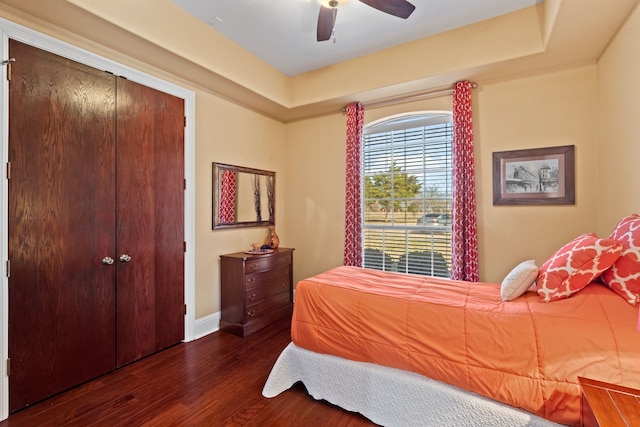 bedroom with dark wood-style flooring, a ceiling fan, baseboards, a closet, and a raised ceiling