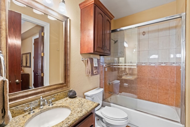 bathroom with a textured wall, shower / bath combination with glass door, vanity, and toilet