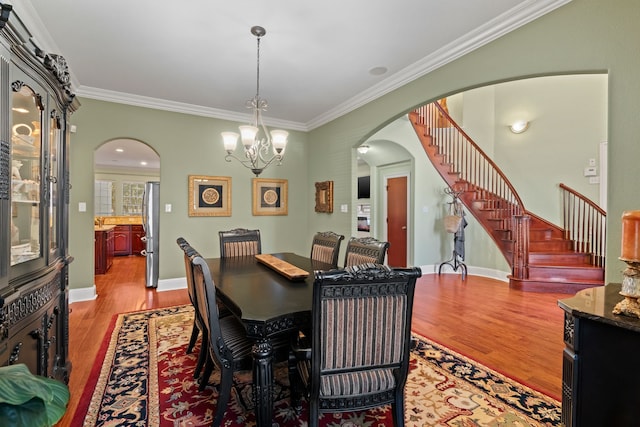 dining area with light wood-type flooring, stairway, arched walkways, and ornamental molding