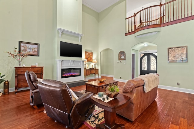 living room with arched walkways, french doors, hardwood / wood-style floors, a glass covered fireplace, and baseboards