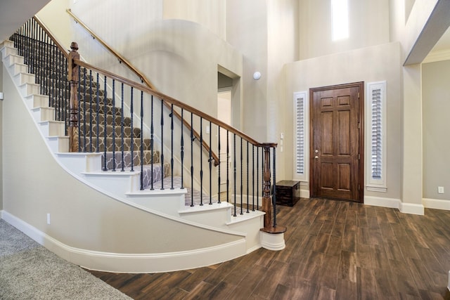 foyer entrance featuring dark wood-style floors, a towering ceiling, and baseboards