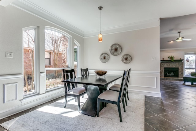 dining space featuring crown molding, dark tile patterned floors, wainscoting, a fireplace, and a decorative wall