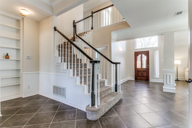 entrance foyer with dark tile patterned floors, visible vents, wainscoting, and ornamental molding