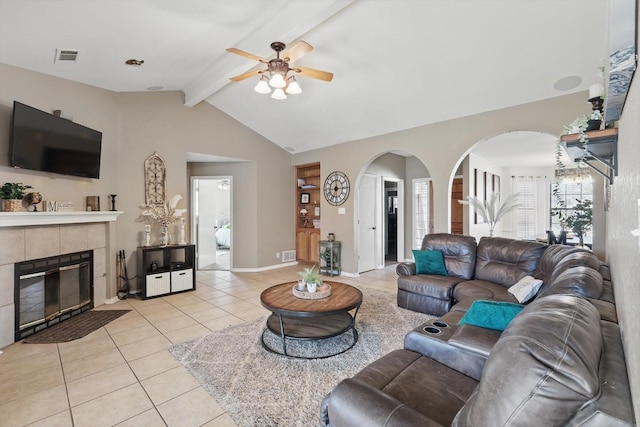 living area featuring arched walkways, a fireplace, lofted ceiling with beams, a ceiling fan, and light tile patterned flooring