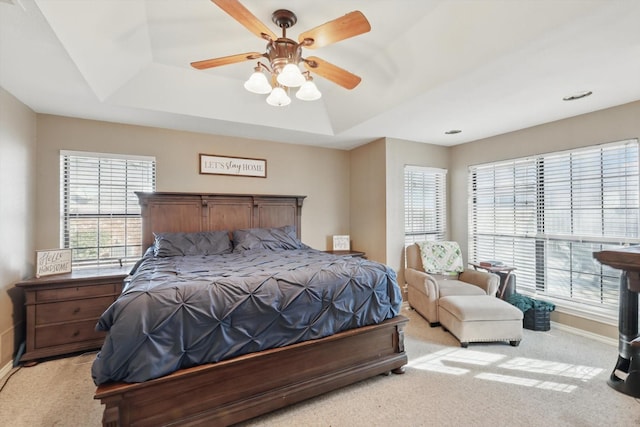 bedroom with a ceiling fan, a raised ceiling, light colored carpet, and baseboards