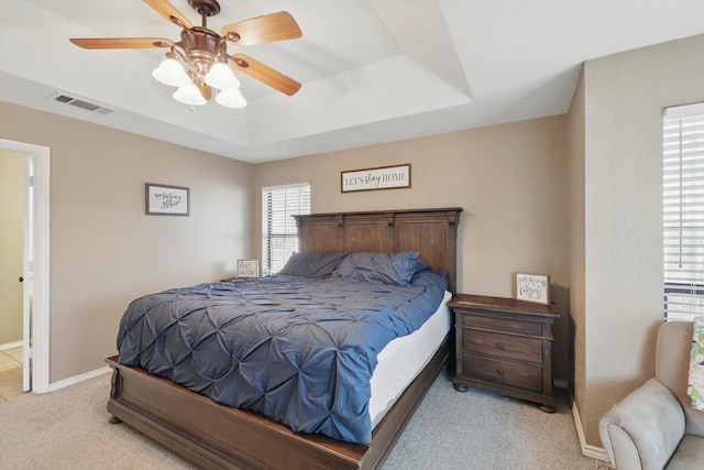 bedroom featuring light colored carpet, a raised ceiling, visible vents, and baseboards