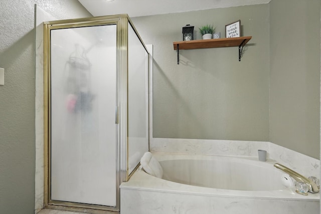 bathroom featuring a stall shower, a garden tub, and a textured wall