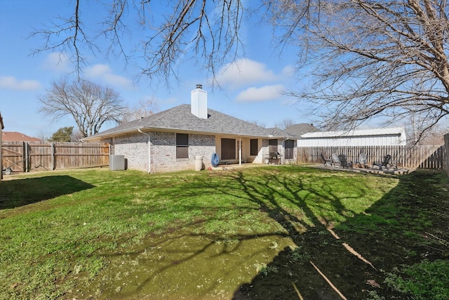 rear view of property featuring a fenced backyard, a chimney, a lawn, and brick siding