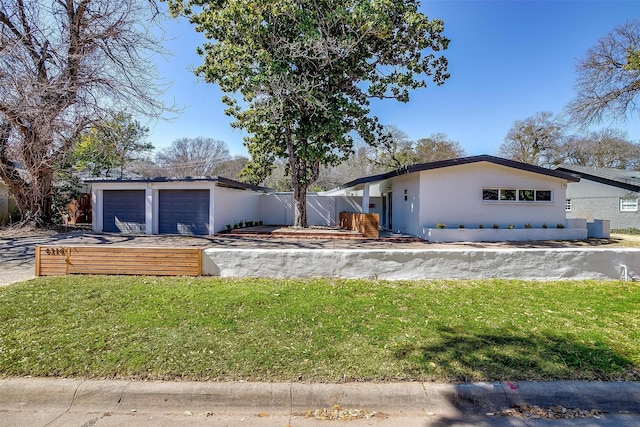 mid-century modern home featuring a garage, a front yard, fence, and stucco siding