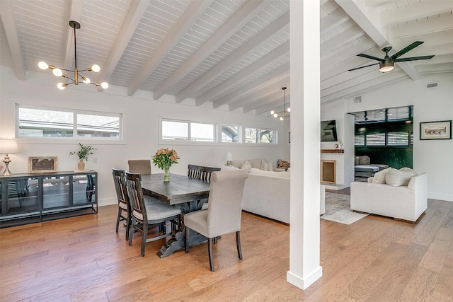 dining room with light wood finished floors, baseboards, visible vents, a fireplace with raised hearth, and lofted ceiling with beams