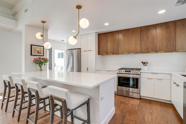 kitchen with white cabinets, light countertops, appliances with stainless steel finishes, a center island, and decorative light fixtures