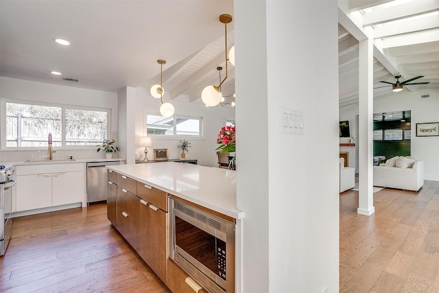 kitchen featuring white cabinets, appliances with stainless steel finishes, light countertops, pendant lighting, and a sink