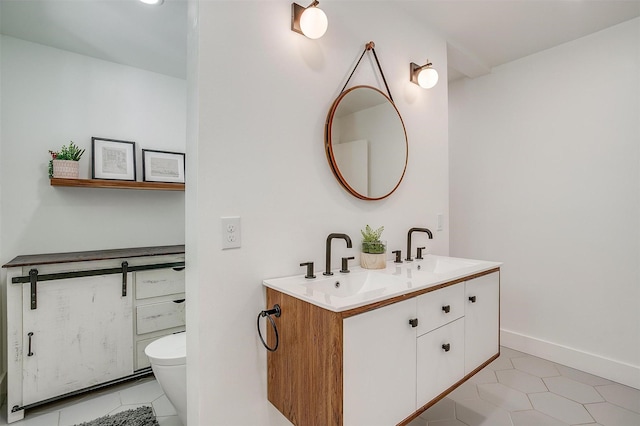 bathroom with baseboards, a sink, toilet, and double vanity