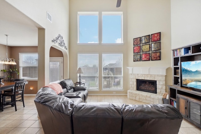 living area with visible vents, a high ceiling, a stone fireplace, light tile patterned floors, and baseboards