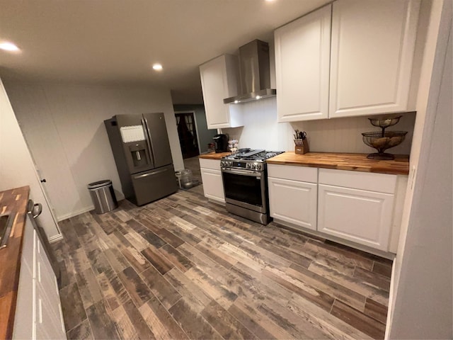 kitchen with appliances with stainless steel finishes, butcher block counters, white cabinetry, and wall chimney exhaust hood