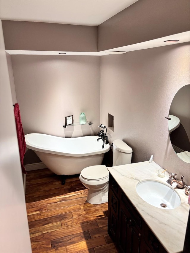 bathroom featuring toilet, a freestanding tub, wood finished floors, and vanity