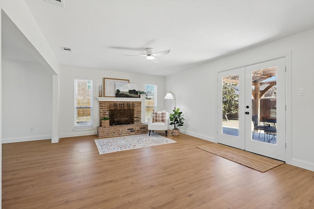 unfurnished living room featuring french doors, a fireplace, light wood finished floors, a ceiling fan, and baseboards