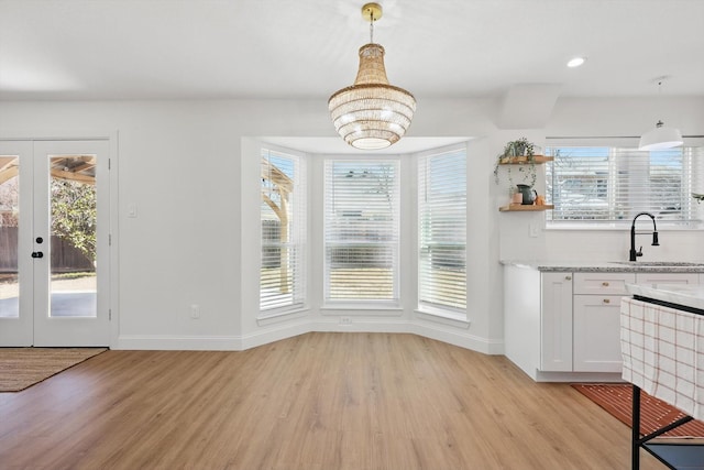 unfurnished dining area featuring french doors, light wood-type flooring, a sink, and baseboards