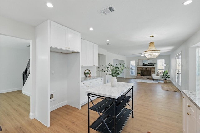 kitchen featuring light wood-type flooring, a fireplace, visible vents, and white cabinetry