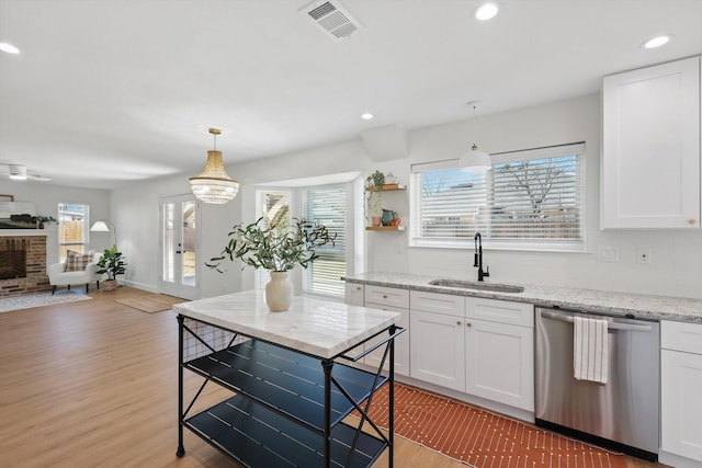 kitchen with a sink, white cabinetry, open floor plan, stainless steel dishwasher, and light wood finished floors