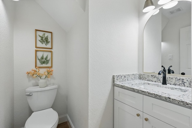 half bathroom with baseboards, visible vents, toilet, vaulted ceiling, and vanity