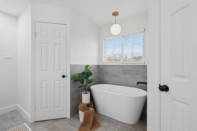 bathroom with tile patterned flooring, a freestanding tub, and tile walls