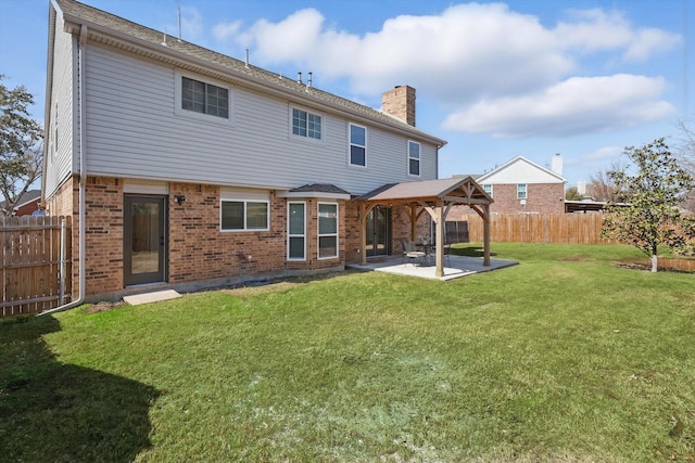 back of property with brick siding, a gazebo, a lawn, a chimney, and a patio area