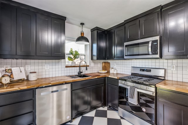 kitchen featuring stainless steel appliances, hanging light fixtures, backsplash, a sink, and butcher block countertops