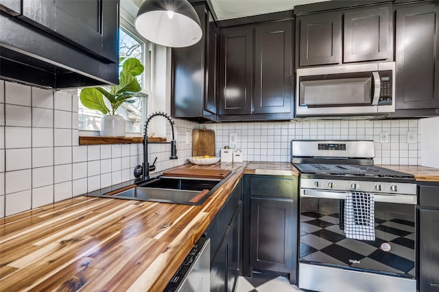 kitchen with butcher block countertops, appliances with stainless steel finishes, backsplash, and a sink