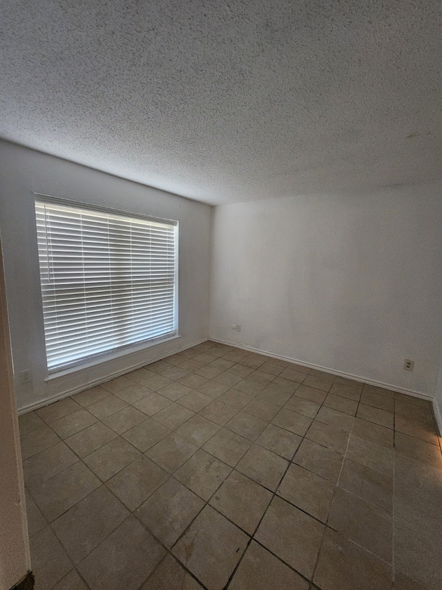 tiled spare room with baseboards and a textured ceiling