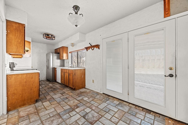 kitchen featuring white dishwasher, stove, light countertops, freestanding refrigerator, and brown cabinets