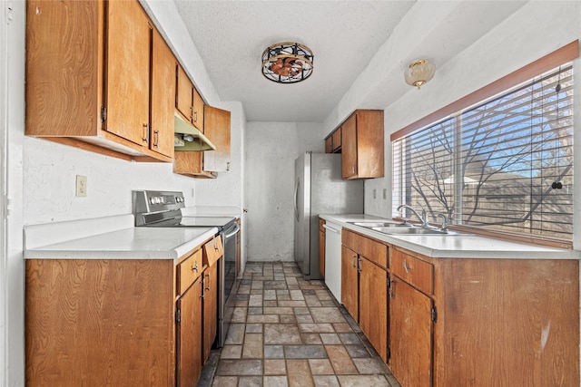 kitchen with brown cabinetry, stainless steel appliances, light countertops, under cabinet range hood, and a sink