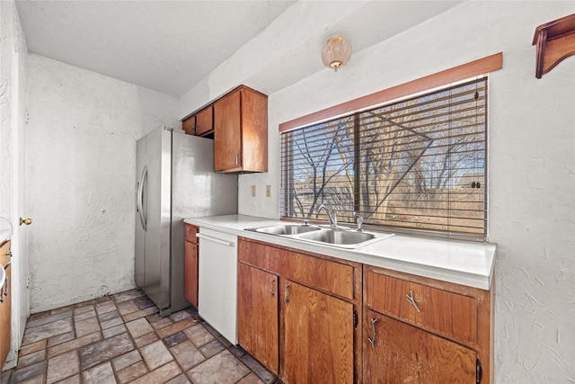 kitchen with dishwasher, light countertops, a sink, and a textured wall