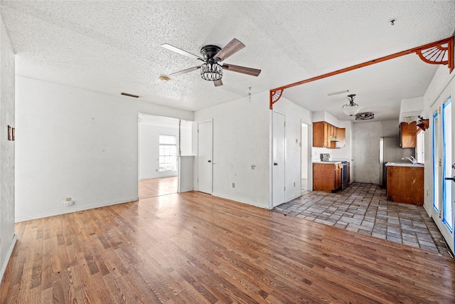 unfurnished living room featuring a ceiling fan, visible vents, light wood-style flooring, and a textured ceiling