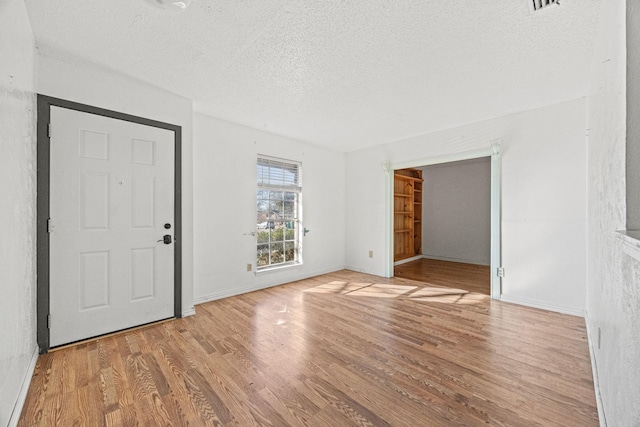 unfurnished room featuring light wood-style flooring, baseboards, and a textured ceiling