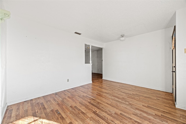 unfurnished room with light wood-type flooring, baseboards, visible vents, and a textured ceiling