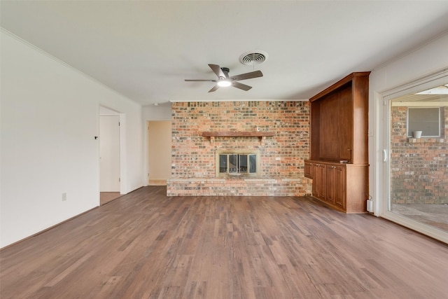 unfurnished living room with visible vents, a fireplace, brick wall, and wood finished floors