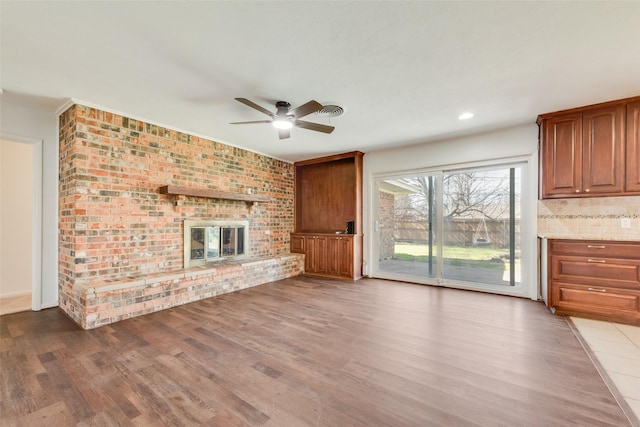 unfurnished living room featuring visible vents, a ceiling fan, brick wall, wood finished floors, and a brick fireplace