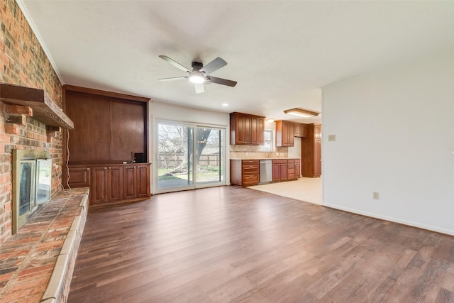 unfurnished living room featuring a ceiling fan, light wood-type flooring, a brick fireplace, and baseboards