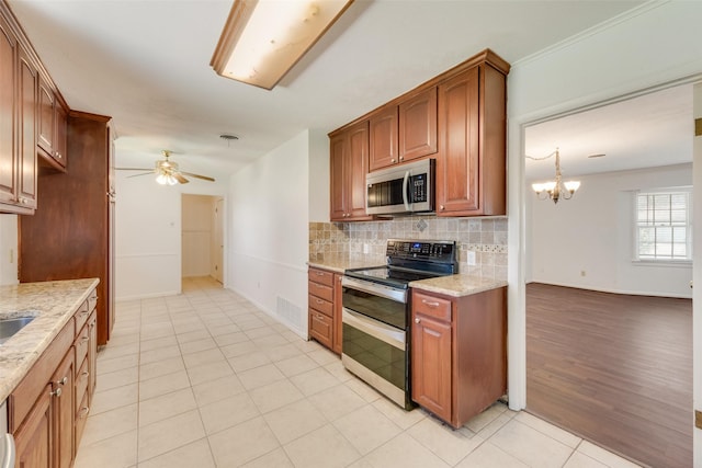 kitchen with brown cabinets, decorative backsplash, appliances with stainless steel finishes, light stone countertops, and ceiling fan with notable chandelier