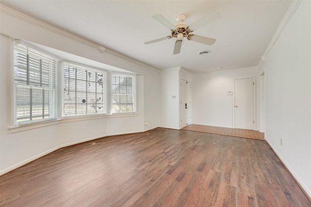 spare room with baseboards, visible vents, ceiling fan, wood finished floors, and crown molding