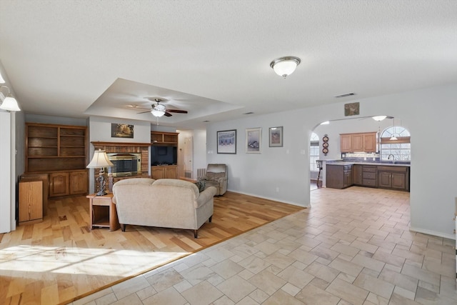living room with arched walkways, ceiling fan, a fireplace, baseboards, and visible vents