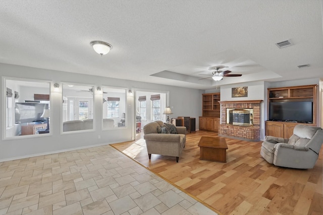 living room with a raised ceiling, a ceiling fan, visible vents, and a textured ceiling