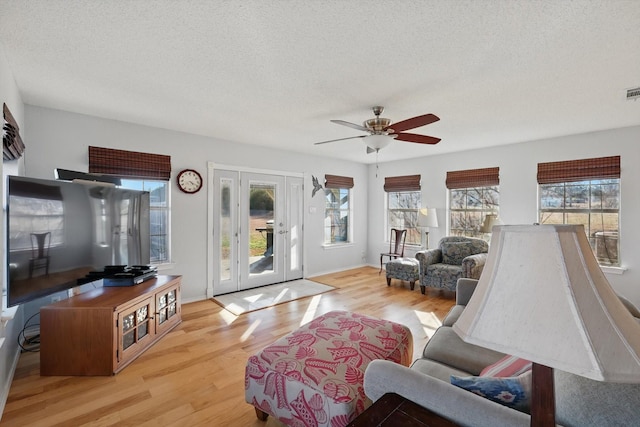 living area with baseboards, light wood-type flooring, ceiling fan, and a textured ceiling