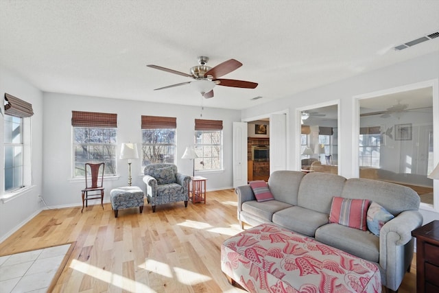 living area with baseboards, visible vents, a ceiling fan, and light wood finished floors