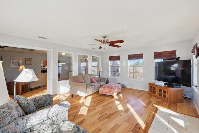 living area with light wood finished floors, a ceiling fan, visible vents, and baseboards
