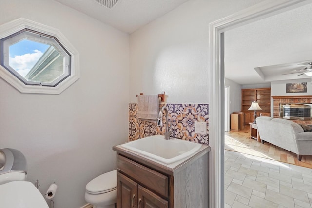 half bathroom featuring vanity, stone finish flooring, toilet, a ceiling fan, and visible vents