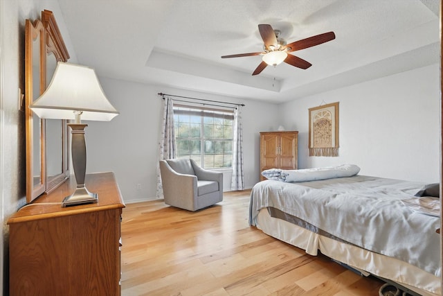 bedroom featuring baseboards, a raised ceiling, a ceiling fan, and light wood-style floors