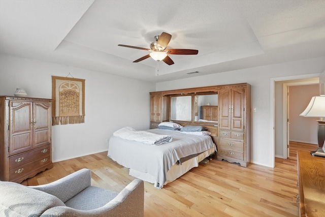 bedroom featuring light wood-style flooring, ceiling fan, baseboards, visible vents, and a tray ceiling